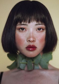 a woman with short hair wearing a black bra and green leaves on her neck is looking at the camera