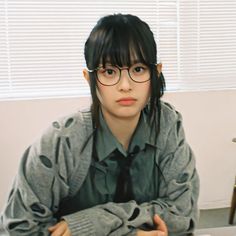 a young woman wearing glasses sitting at a desk with her arms crossed and looking off to the side