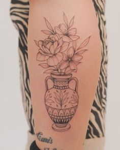 a woman's leg with a vase and flowers tattoo on the side of her thigh