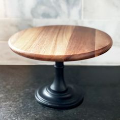 a wooden cake plate sitting on top of a black counter next to a white tile wall