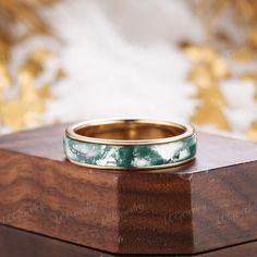 a wedding band with green marble inlays sits on top of a wooden box