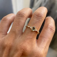 a woman's hand wearing a gold ring with an oval shaped green stone on it