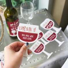 a person holding up a wine bottle sticker with the words drink me on it