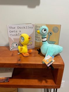 two stuffed animals sitting on a wooden table next to a bookshelf and book