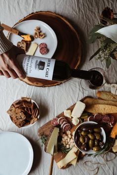 a table topped with cheeses, crackers and olives next to a bottle of wine