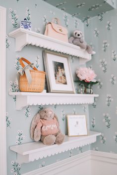 two white shelves with stuffed animals and pictures on them in a blue wallpapered room