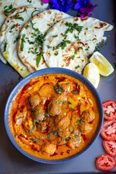 some food is in a blue bowl on a table next to sliced tomatoes and pita bread