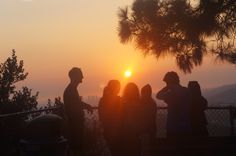 the sun is setting behind some people on a hill