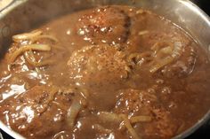 meatballs and onions are being cooked in a pot on the stove top with gravy