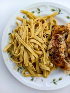 a white plate topped with pasta and chicken next to a piece of meat covered in sauce