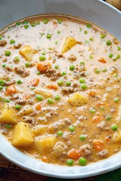 a white bowl filled with soup and potatoes on top of a wooden table next to bread