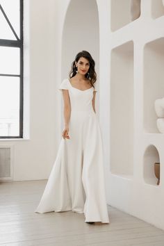 a woman standing in front of a wall wearing a white dress