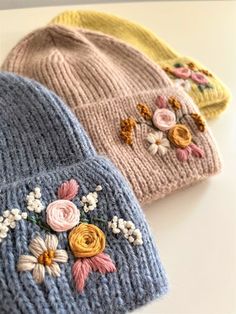 three knitted hats with flowers on them