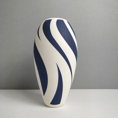 a white and blue vase sitting on top of a table next to a gray wall