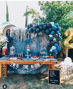 an outdoor party setup with balloons, streamers and food on the table for two to the moon