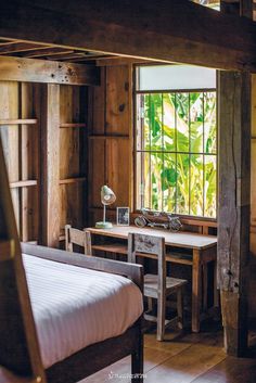 a bed and desk in a room with wood paneled walls, windows and wooden flooring