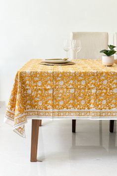 a yellow table cloth with white flowers on it and two wine glasses sitting on the table