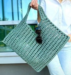 a woman holding a green crocheted bag in front of a window with sunglasses on it