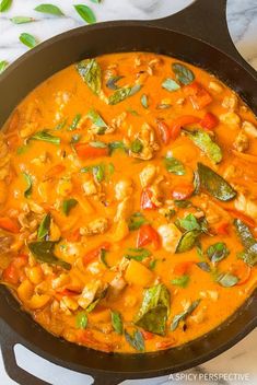 a skillet filled with chicken and vegetables on top of a marble counter next to green leaves