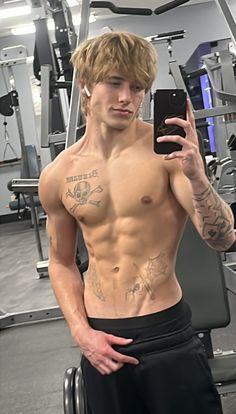 a shirtless man taking a selfie with his cell phone in a gym room