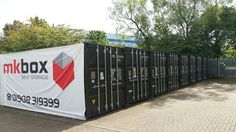 a group of black shipping containers sitting next to each other on a brick walkway in front of trees