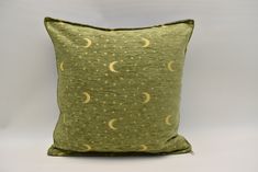 a green pillow with yellow stars and crescents on the front, sitting against a gray background