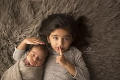 two young children laying on top of each other with their fingers up to their mouths