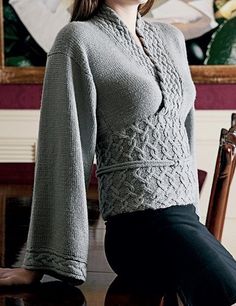 a woman standing in front of a table wearing a gray sweater and black pants with her hands on her hips