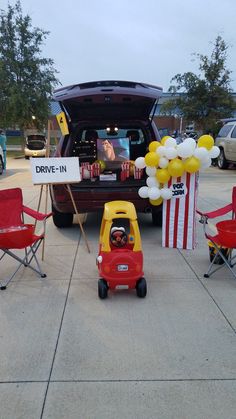 a little red car is parked in front of a drive - in with balloons and decorations