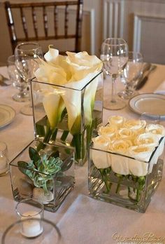 two vases filled with flowers on top of a table next to wine glasses and silverware