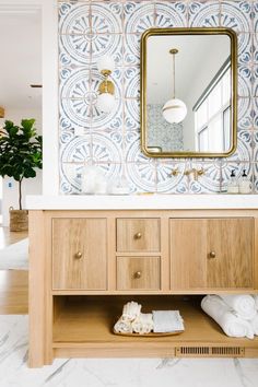 a bathroom with blue and white tiles on the wall, wooden cabinets and a gold framed mirror