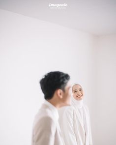 a man and woman standing next to each other in front of a white wall smiling