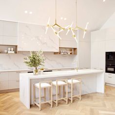 a white kitchen with marble counter tops and wooden stools next to an island in the middle