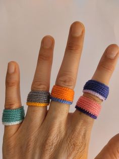 a person's hand with four different colored rings on their fingers and one is holding something in the other hand