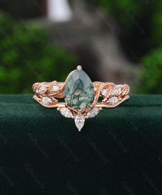 an engagement ring with a green stone and white diamonds on the side, sitting on top of a velvet surface