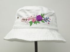 a white hat with flowers and leaves embroidered on the brim, sitting on a stand