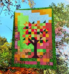 a quilt hanging from a tree with leaves around it