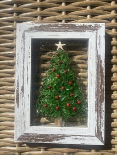 a small christmas tree in a white frame on a wicker wall with red berries