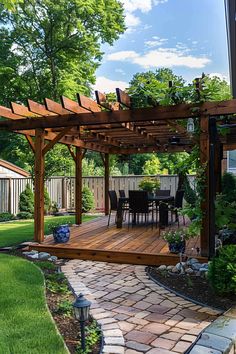 Wooden pergola on a backyard deck with outdoor dining set. Paved pathway leads to the deck, surrounded by lush greenery and decorative plants. Back Porch With Pergola, Decks With Pergolas And Fire Pit, Landscaping Around Pergola, Pergola Off The House, Wood Deck With Pergola, Pergola Accessories Outdoor, Shade Structure Backyard, Garden Living Room Outdoor, Backyard Patio Designs Small Yard