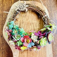 a close up of a wreath on a wooden board with succulents in it