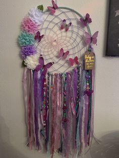 a dream catcher with flowers and butterflies hanging from it's side on a wall