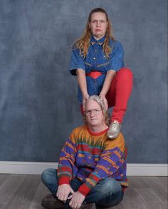 two people sitting on top of each other in front of a blue wall and wooden floor