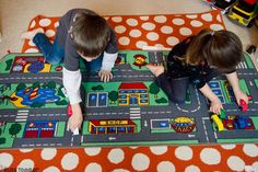 two children playing on a play mat with cars and trucks in the street area at home