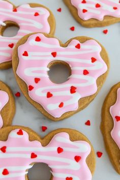 heart shaped donuts with pink frosting and sprinkles on a white surface