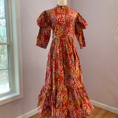 This Is A Never-Worn Sika Designs Brand Dress Made Of Beautiful 100% Cotton Batik Hand Made In Ghana. The Dress Has A Red Background, With Yellow, Gold And Blue Floral Design. The Sleeves Have An Interesting Fluttery Part Atop The Long Sleeve Itself, Making The Dress Look Victorian To Me. The Dress Buttons Down From The Mandarin Collar To The Flouncy Hem, And Has Side Seam Pockets, Plus A Sash. This Dress Has Volume, And Is A Uk Size 12. The Dress Is 50 In Long From Neckline To Hem; Please Double The Following: 15 In Waist, 17.5 In Pit To Pit, Hips Are Free Size Due To The Elegant Flare Of The Dress From The Waist. Fitted Ikat Print Dress, Red Fitted Dress With Batik Print, Fitted Red Dress With Batik Print, Red Long Sleeve Dress With Batik Print, Red Cotton Batik Print Dresses, Red Long Sleeve Dresses With Batik Print, Red Cotton Dress With Batik Print, Fitted Block Print Maxi Dress, Red Fitted Block Print Dress