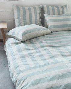 a bed with blue and white striped comforter on it's headboard next to a night stand