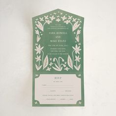 a green and white wedding card with floral designs on it's front, in the shape of a hexagonal frame