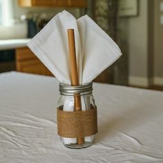 a mason jar with two wooden utensils in it sitting on a white bed