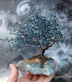 a hand holding up a rock with a tree on it and blue crystals in the middle