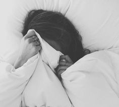 black and white photograph of a woman sleeping in bed with her head under the covers